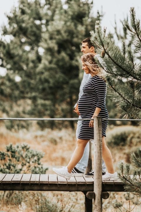 Pregnant woman, with swollen ankles due to pregnancy, holding hands with a man while they are walking on a bridge